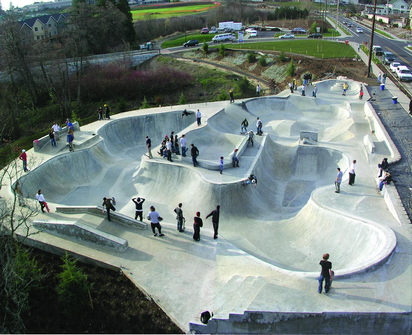 Tanner Creek Park from above: connected bowls terraced into the hillside above West Linn, riders spread across the decks and the road along the top edge.