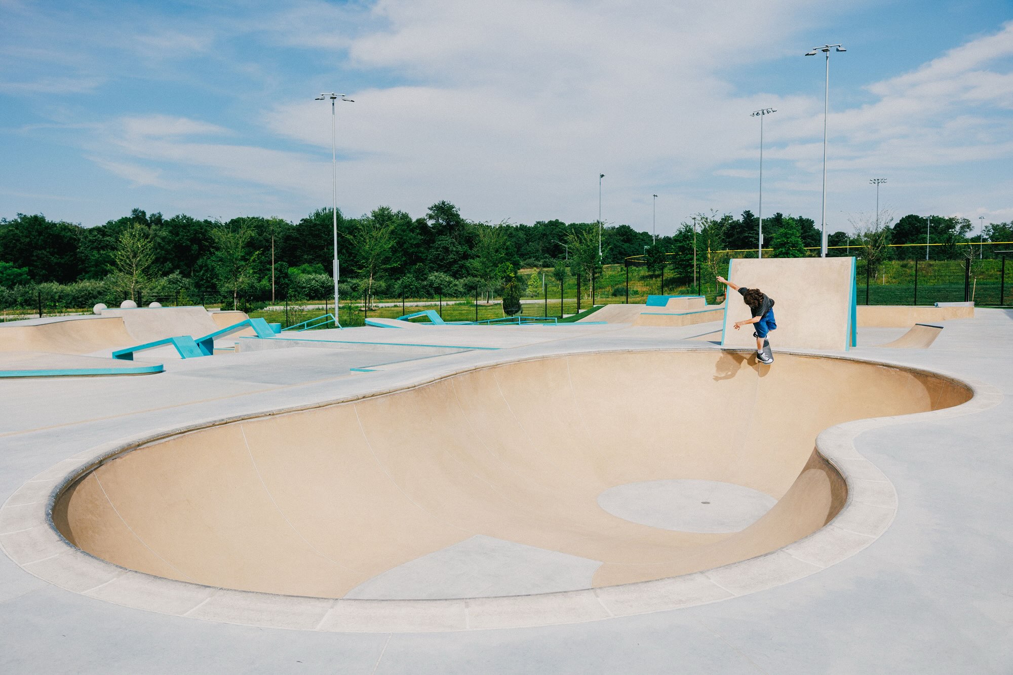 A skater on the coping of the big bowl at Blandair, with the teal-trimmed street course and the light poles behind.