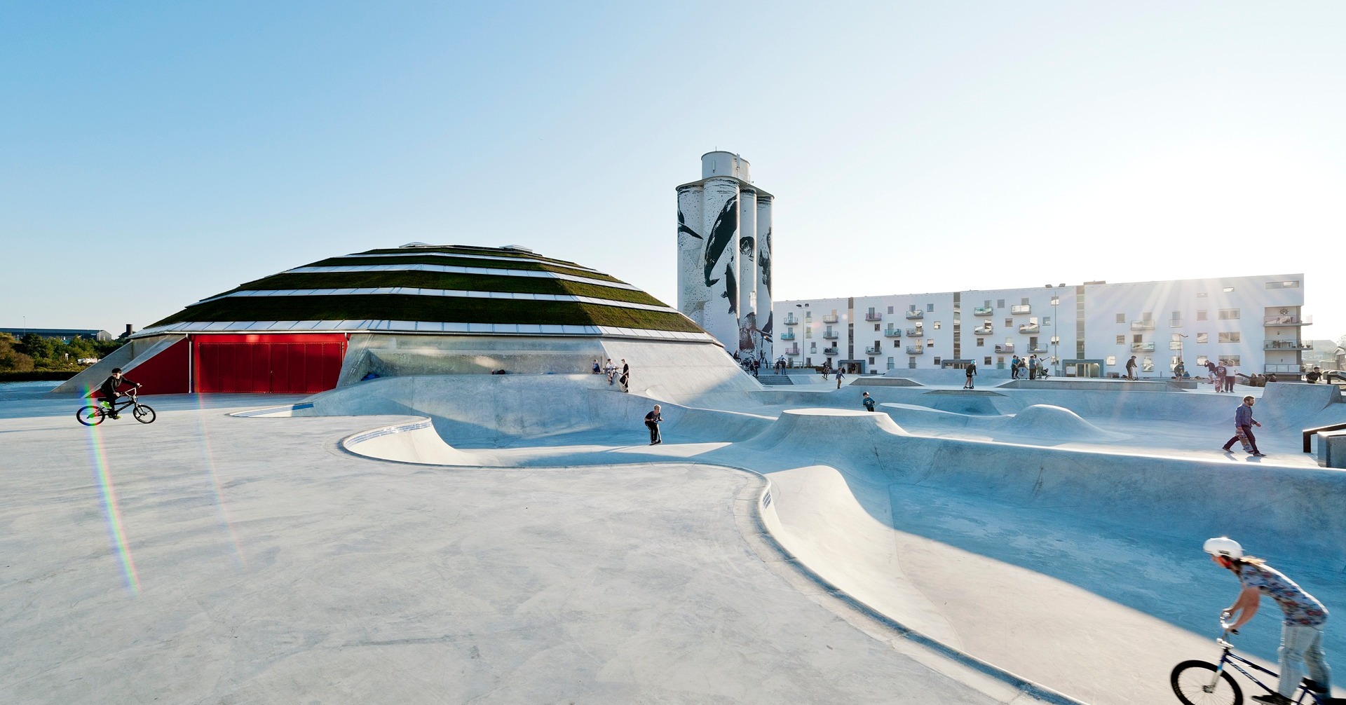 The StreetDome in Haderslev, Denmark: Grindline's concrete bowls and banks flow up to the dome building, a BMX rider drops in at the left edge, and apartment blocks stand behind.