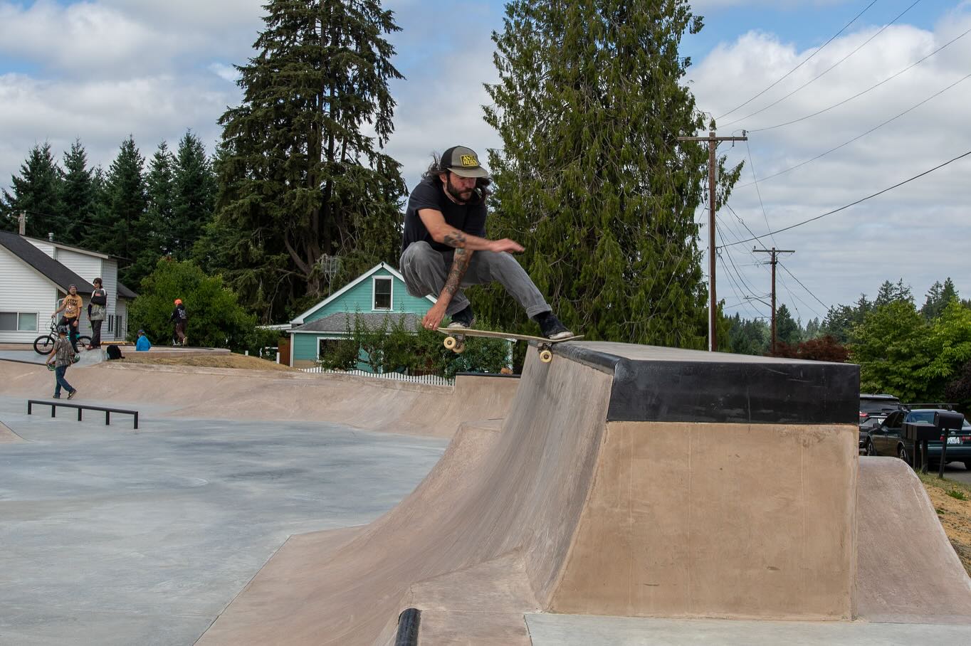 A skater riding the hubba over the bank at KJ Gardner Skatepark in Black Diamond, with the bowl and the street plaza behind.