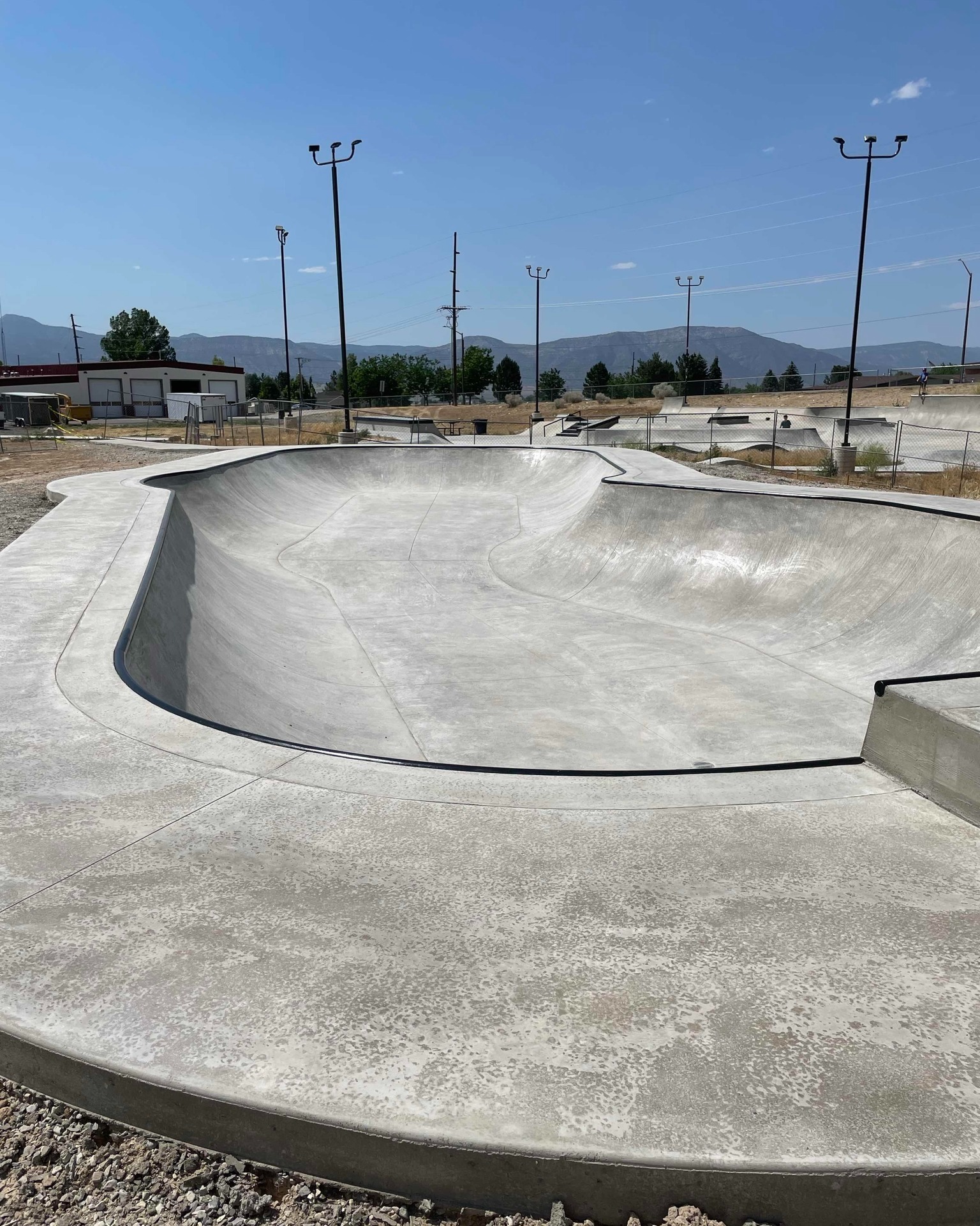 The phase-two bowl at Ephraim Skatepark, fresh concrete with black coping, light poles around it and the mountains of Sanpete County behind.