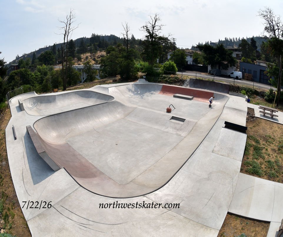 Jacob's Skatepark in Mosier from above, the whole bowl with its rust-red wall, a skater on the far side and the wooded Columbia River Gorge hills behind.
